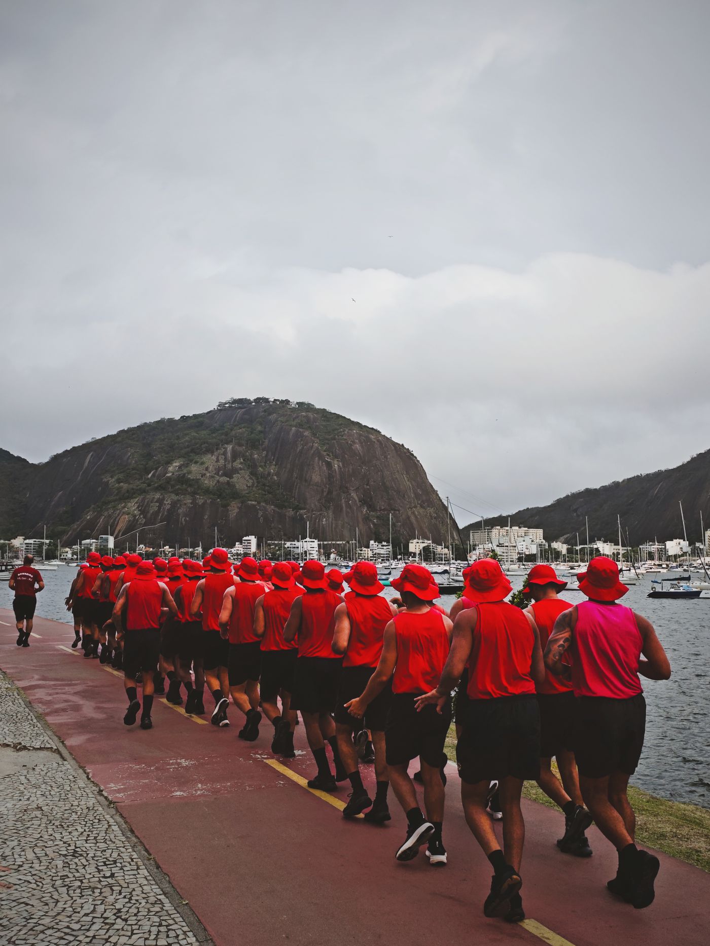 Grupo de corredores em roupas vermelhas treinando junto à orla no Rio de Janeiro